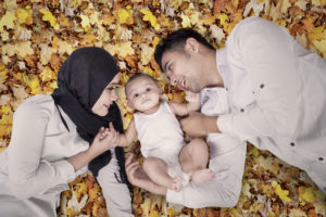 Image of cute male baby lying on the autumn leaves with his parents