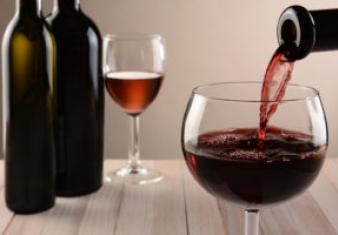 Closeup of a glass of wine and a bottle pouring. Out of focus wine bottles and another wineglass are in the background. Horizontal still life with warm tones and light to dark background lighting.