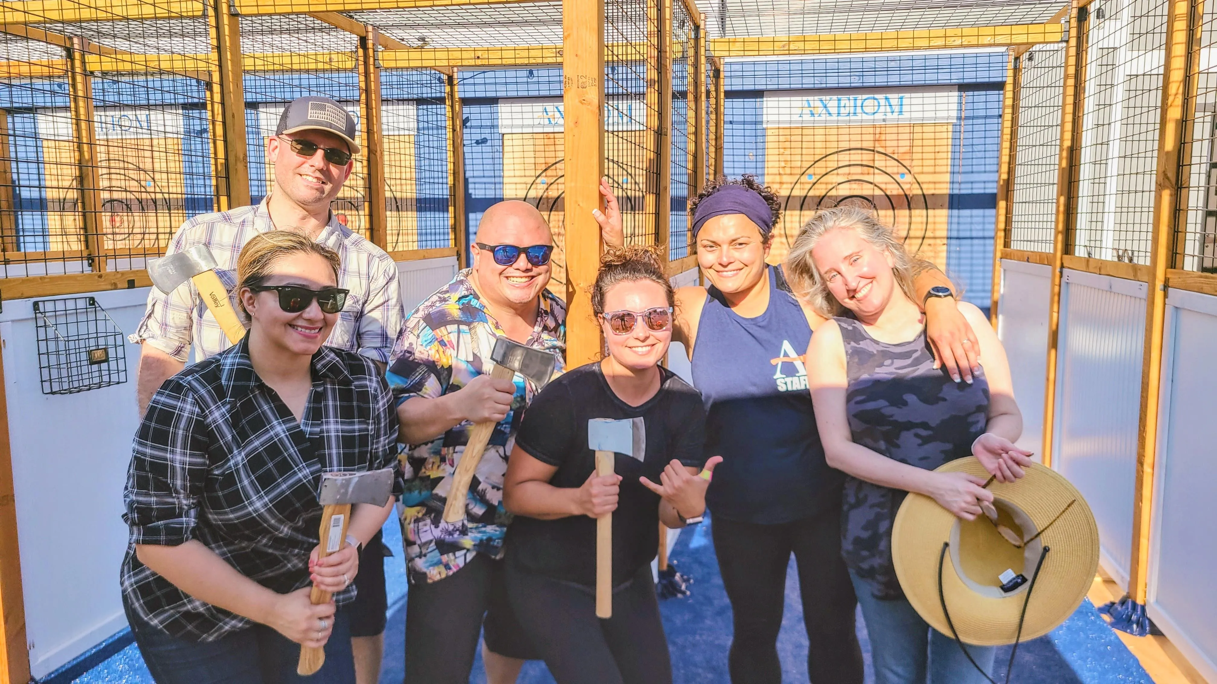Group photo of Carly Johnstone and Axeiom guests, smiling and holding axes, in front of axe throwing targets.