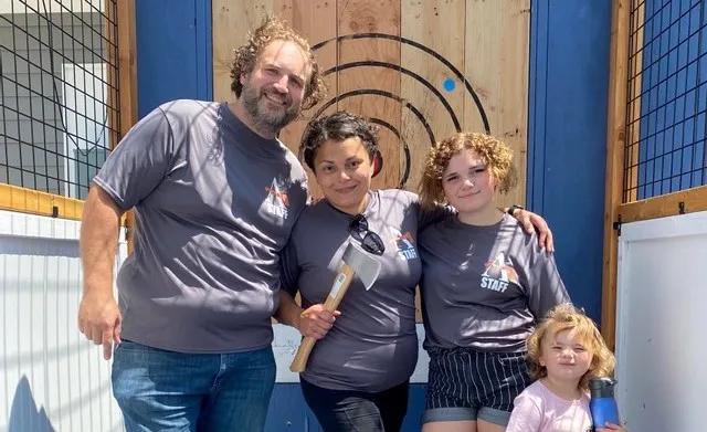 Johnstone family, smiling and standing, in front of Axeiom axe throwing targets.