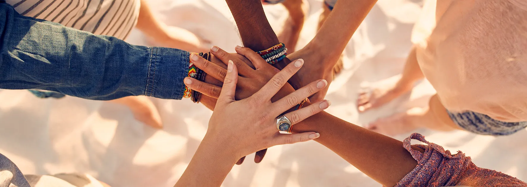 Image of a group of people with their hands stacked in the center on the beach.